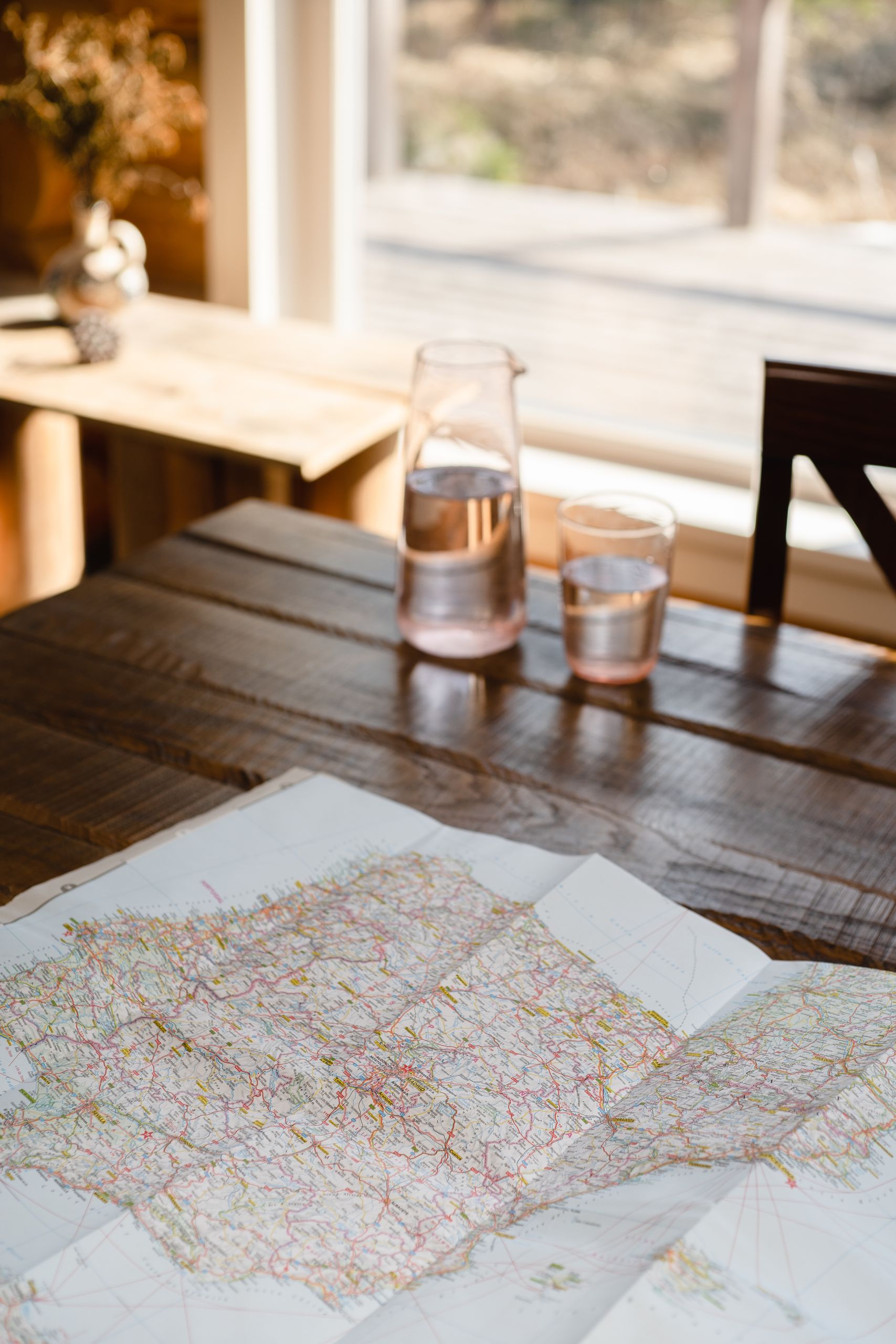A serene indoor setting with a glass pitcher, map, and natural lighting on a wooden table.