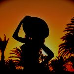 Stunning silhouette of a woman wearing a hat against a vibrant sunset sky with palm trees.